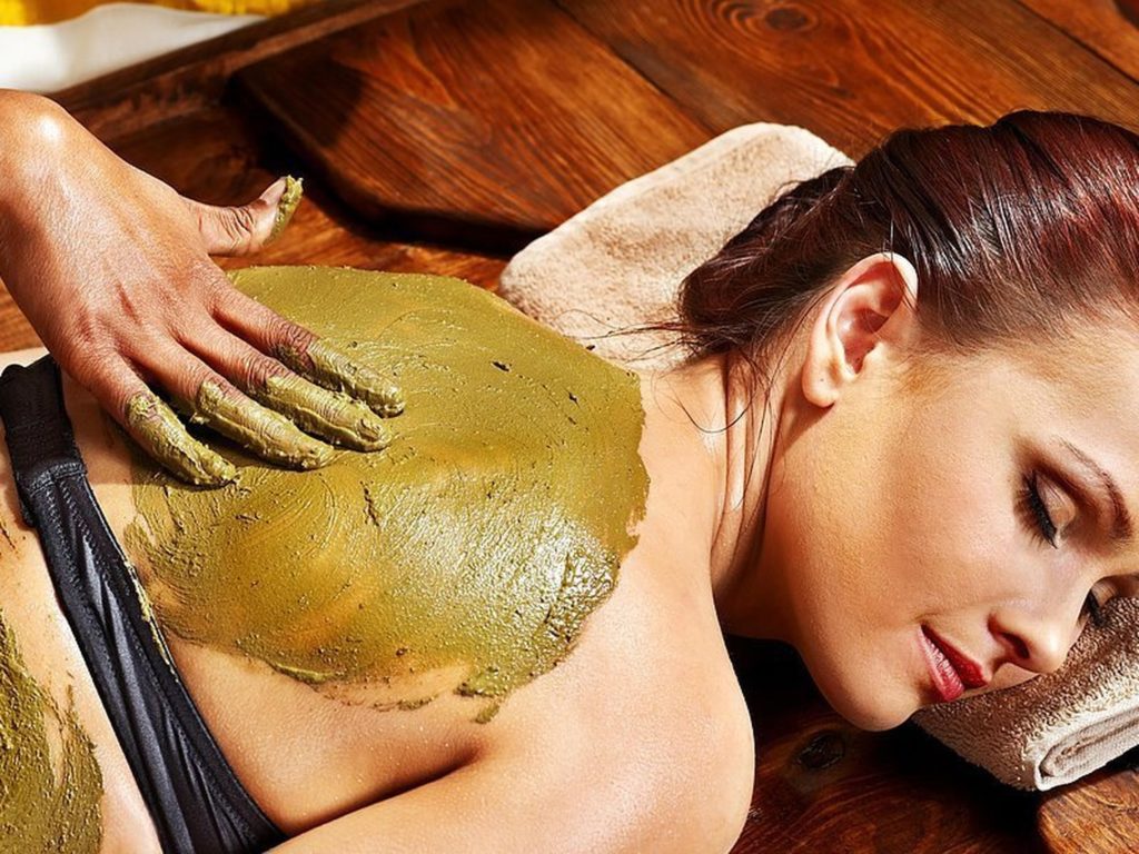 a massage therapist applying a clay mask on a clients back 
